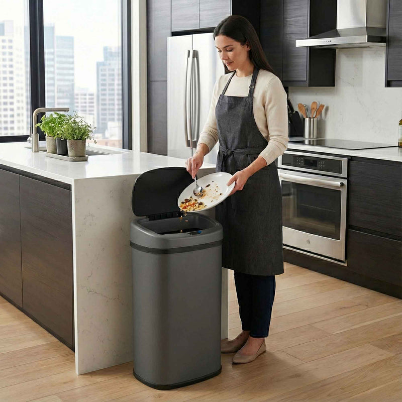 A woman in a modern kitchen using the iTouchless ITOS13GY gray stainless steel 50L sensor trash can to throw garbage away.