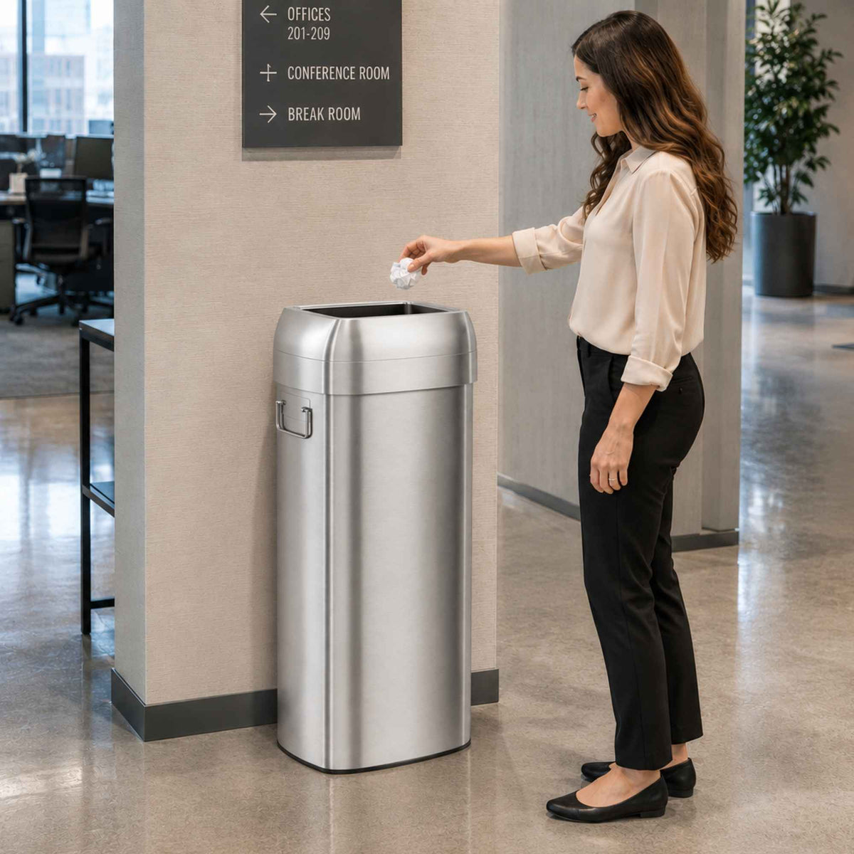 Woman disposing waste in iTouchless 30 gallon open top trash can in office corridor near conference room and break room
