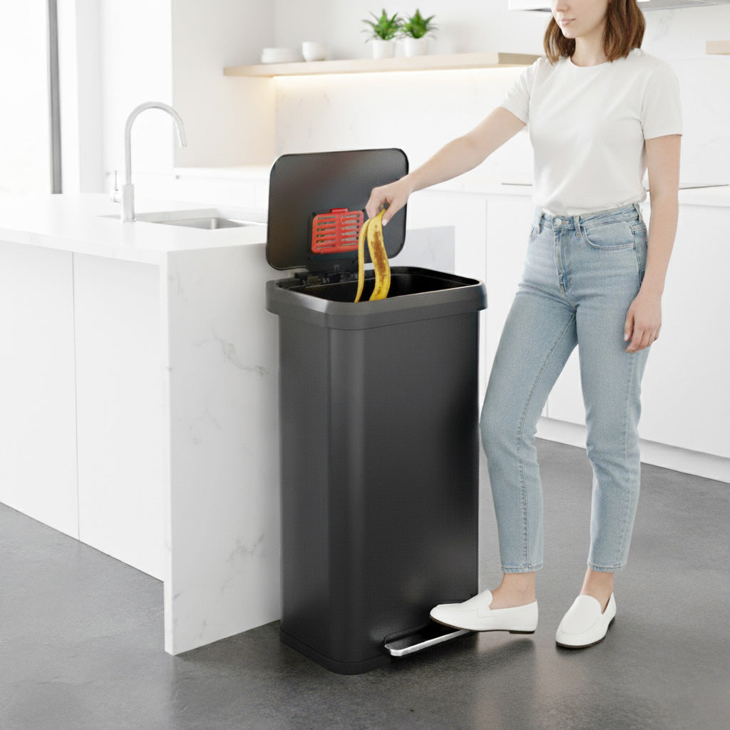 A woman in a modern kitchen using the iTouchless PP20RSGY gray stainless steel 75L step trash can to throw garbage away.