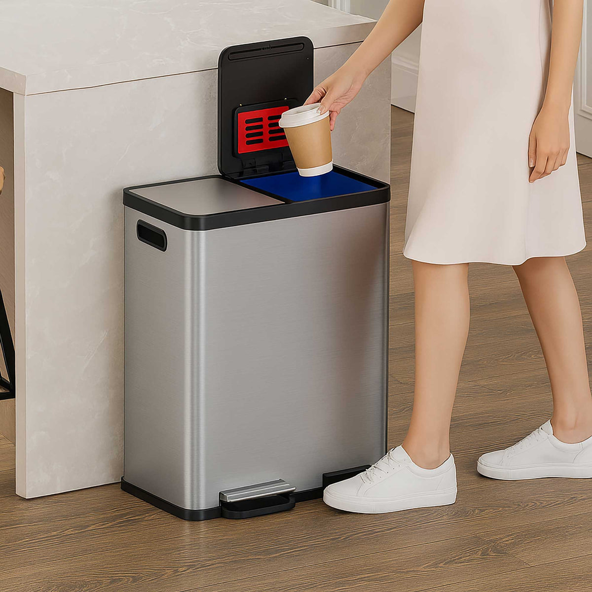 A woman in a modern kitchen using the iTouchless PC60RSS stainless steel 60L step trash can to sort a paper cup into one of the recycling compartments.
